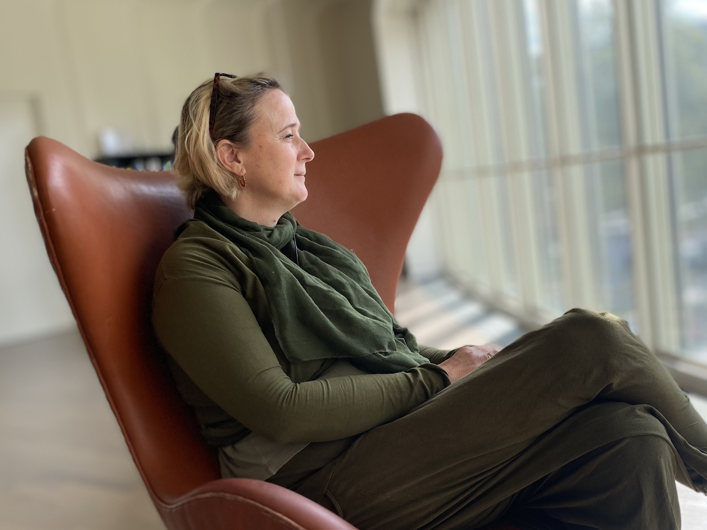 Vrouw met MS neemt rust in een leren fauteuil en kijkt ontspannen naar buiten